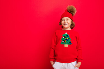 cheerful funny boy on a red background in a warm hat and sweater with a Christmas tree