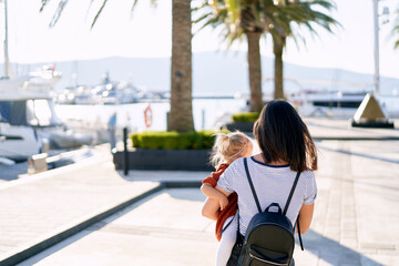 Mother is carrying her baby girl in her arms on a boat pier in Porto Montenegro