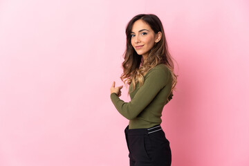 Young caucasian woman isolated on pink background pointing back