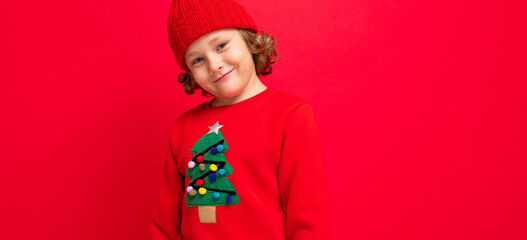 cool boy with curls on a red background in a sweater with a christmas tree