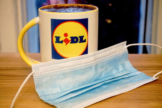 Riga, Latvia - november 13, 2020:White mug with coffee and store chain LIDL logo, in the foreground covid 19 face protection mask.