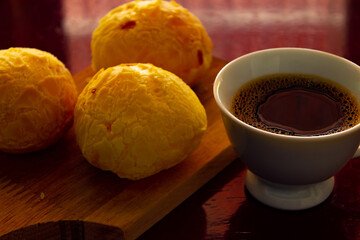 Xícara branca de café e pães de queijo sobre superfície reflexiva.