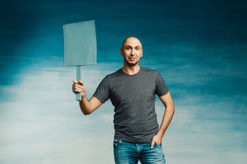 Attractive bald man in a T-shirt with a protest poster in his hands on a blue background