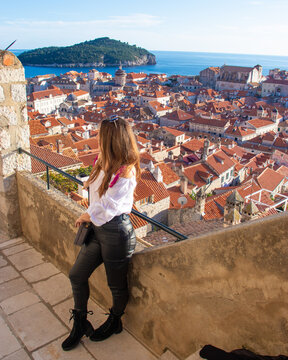 Attractive brunette influencer standing on the city walls of Dubrovnik, posing for a vertical photo for social media. Rooftops of the old city in the background on a bright autumn day