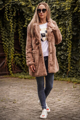 Fototapeta premium Young blond-haired fashion model takes photos for a fashion store outdoors with a blurred background.