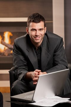 Businessman working from home with laptop in home office by fireplace