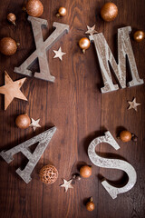 Silberne XMAS Buchstaben in warmen gold- und braun Tönen auf Holz mit goldenen Weihnachtskugeln...