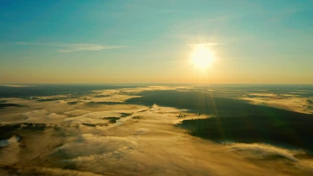 Drone is panning above beautiful morning landscape with a fog while golden sunrise. Aerial view of sunrise with fog in blue sky above river Desna, Ukraine.  Huge water evaporation over the lake.