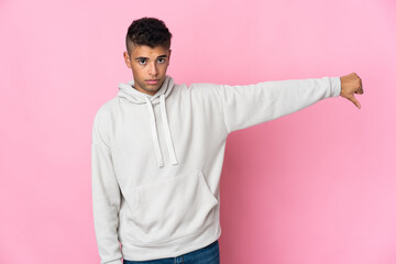Young Brazilian man isolated on pink background showing thumb down with negative expression