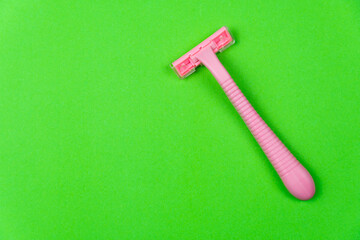 Pink disposable razor on a green background, free space for text