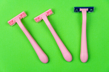 Three pink disposable razors on a green . Personal hygiene items for shaving.