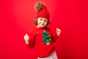 cheerful funny boy on a red background in a warm hat and sweater with a Christmas tree
