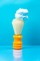 Fototapeta na wymiar Shaving foam on an orange shaving brush on a blue background.