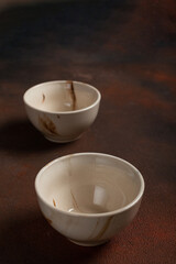 Two light handmade cups on a brown background