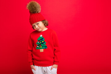 cheerful funny boy on a red background in a warm hat and sweater with a Christmas tree
