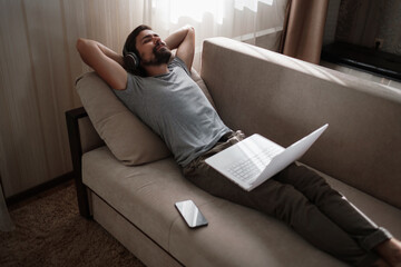 Man on sofa with headphones and notebook at home