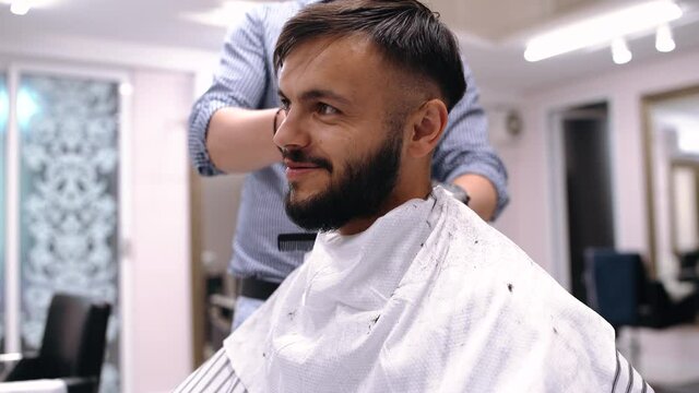 Young man in barber shop sits in an armchair. Barber cuts his hair with a trimer