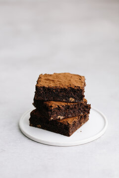 Stack of 3 brownies on plate with cocoa powder dusted
