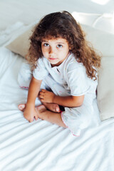 Naklejka premium Beautiful little curly girl in the bedroom on the bed
