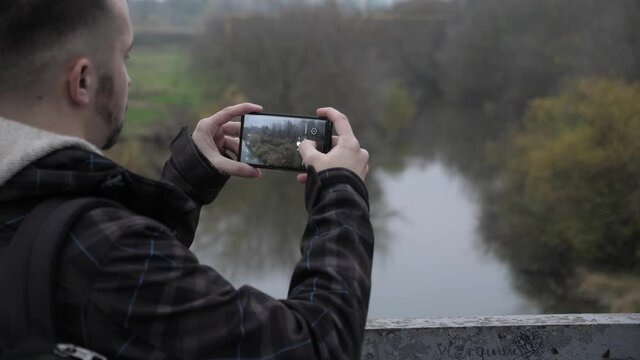 Young guy takes pictures from the phone of beautiful nature, autumn, cold weather