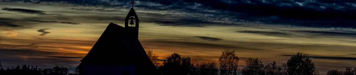 Panorama, Umrisse einer Kirche und Silhouetten von Bäumen vor einem Sonnenuntergang Himmel