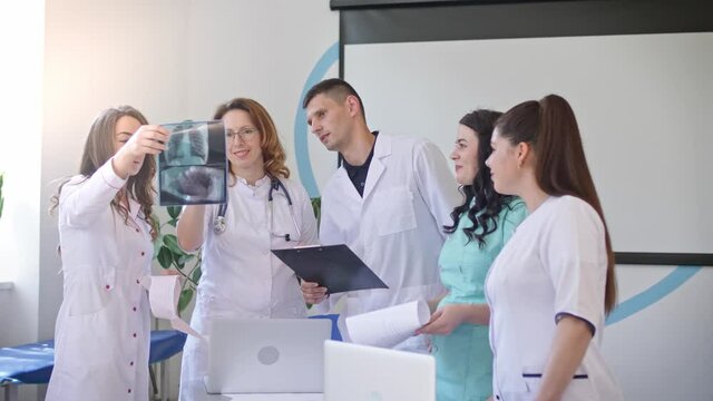 Female Doctor and Young Medical Interns in Medical Clothing Studying Together the Results Chest X-Ray Scan of Patient. Middle-Aged Woman Therapist Teaching Young Interns How to Analyze X-Ray Image