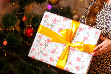 Gift box with a bow in female hands on the background of a Christmas tree.