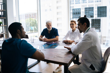 Medical team of professional doctors on meeting in medical office discussion about new treatment for patient sitting at the desk in modern conference office room. Concept of medicine and health care.