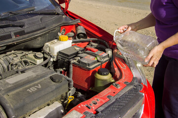 Woman pouring water into the tank of a car