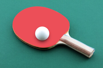 Green ping pong table with ball resting on a table tennis bat paddle