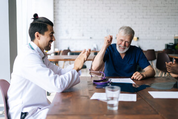 Friendly multi-ethnic team of doctors congratulate happy mature male physician leader winner applaud in office. Cheerful mixed ethnic colleagues applauding. Concept of medicine and health care.