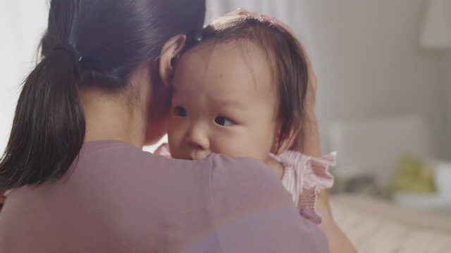 Close up shot of affectionate Asian mother holding baby girl on arms, cuddling and kissing her with love