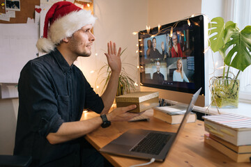 Remote Christmas video party. Family quality time during pandemic. Online video call conferencing. Young man wearing red Santa hat and holding a gift box. Virtual meeting conference calling from home