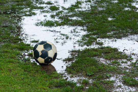 Worn soccer ball on a wet field with puddles in the rain