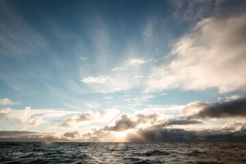 Sunset beams through white clouds above rippled ocean water