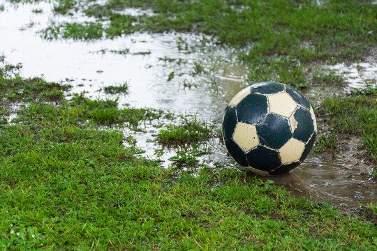 Worn soccer ball on a wet field with puddles in the rain