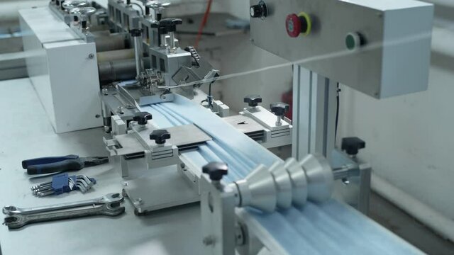 Production of medical three-layer whites. Manufacturing of protective face masks during the coronavirus pandemic. The plant makes face masks for the virus. The machine creates clothes for doctors.