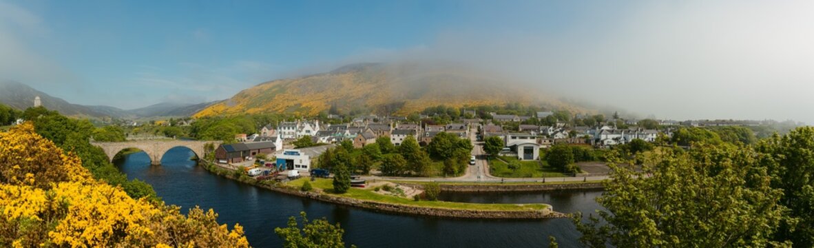 Breathtaking scenery with small old town on shore of calm river at foothill of misty mountain