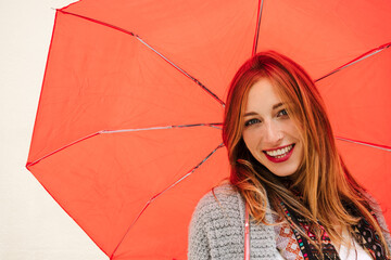 Close-up of a young blonde girl smiling at the camera while standing under a red umbrella.