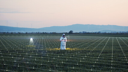 Farmer man in white protective suit using innovation device for working on farm field in dusk....
