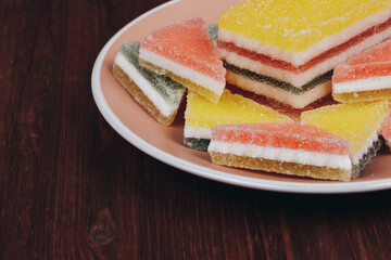 Colorful jelly candy in the plate on wooden background. Multi-colored marmalade jelly candy's. Heap of triangular and rectangular  marmalade candy.