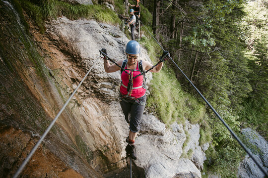Sportive female alpinist walking tightrope in mountains in summertime