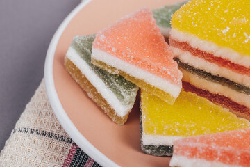 Colorful jelly candy in the plate at checkered napkin on grey background. Multi-colored marmalade jelly candy's. Heap of triangular and rectangular  marmalade candy.
