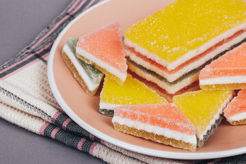 Colorful jelly candy in the plate at checkered napkin on grey background. Multi-colored marmalade jelly candy's. Heap of triangular and rectangular  marmalade candy.