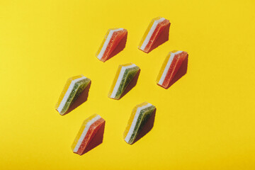 Set of colorful triangular jelly candy lined up on yellow background. Multi-colored marmalade jelly candy's. Top view.