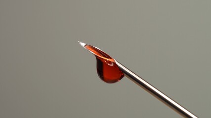 Drops of blood from the tip of the medical syringe. Bloody liquid dripping from needle, macro close...