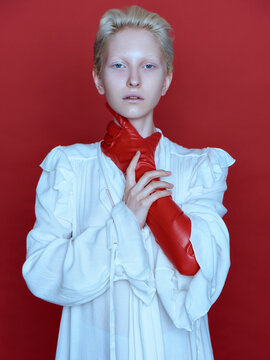 Fashionable portrait of an albino model who strangles herself with her hand in a red glove