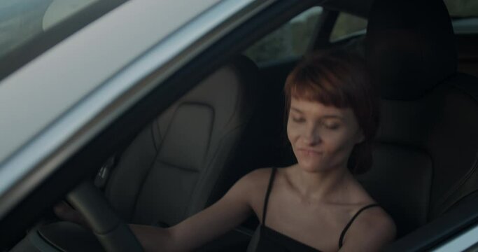 Cute girl in her electric car, listening to music and dancing on the driver's seat. Handheld video
