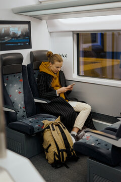 woman with a bagpack and Luggage is sitting on a high-speed train to the airport. she holds a smartphone in her hands and writes to her parents and friends that she is flying home