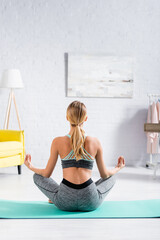 Back view of sportswoman meditating on floor in living room